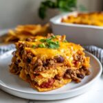 A slice of Easy Doritos Casserole Recipe on a white plate, layered with Doritos, meat, beans, and melted cheese.