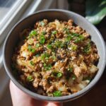 A bowl of Egg Roll Bowls with Chicken and Cabbage, garnished with sesame seeds and green onions.