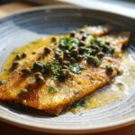 Pan-fried fish fillet topped with vibrant Lemon Caper Sauce and fresh herbs on a plate.