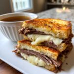 A stacked French Dip Grilled Cheese sandwich with melted cheese and a side of au jus.