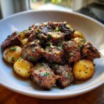 A bowl of Garlic Butter Beef Bites and Potatoes, garnished with fresh herbs and garlic.