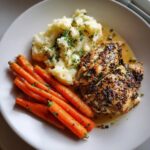 A plate of Garlic Herb Chicken with Mashed Potatoes and Glazed Carrots, garnished with fresh herbs.