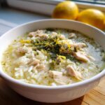 A bowl of Classic Greek Lemon Chicken Soup with rice, chicken, herbs, and lemon zest.