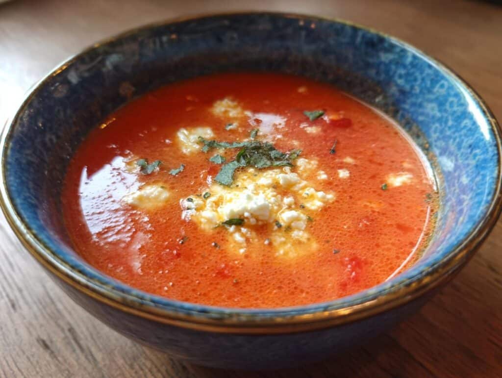 A bowl of High Protein Tomato Soup with Cottage Cheese, garnished with fresh herbs.