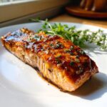 A delicious piece of Honey Pineapple Glazed Salmon on a white plate, garnished with fresh herbs.
