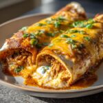 Two Jalapeño Popper Chicken Enchiladas on a plate, topped with cheese, jalapeños, and cilantro.
