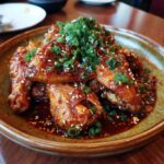 Close-up of Korean Chicken Recipe wings with sesame seeds and green onions on a plate.