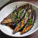 A bowl of Miso Glazed Eggplant, garnished with sesame seeds and fresh herbs, ready to be served.