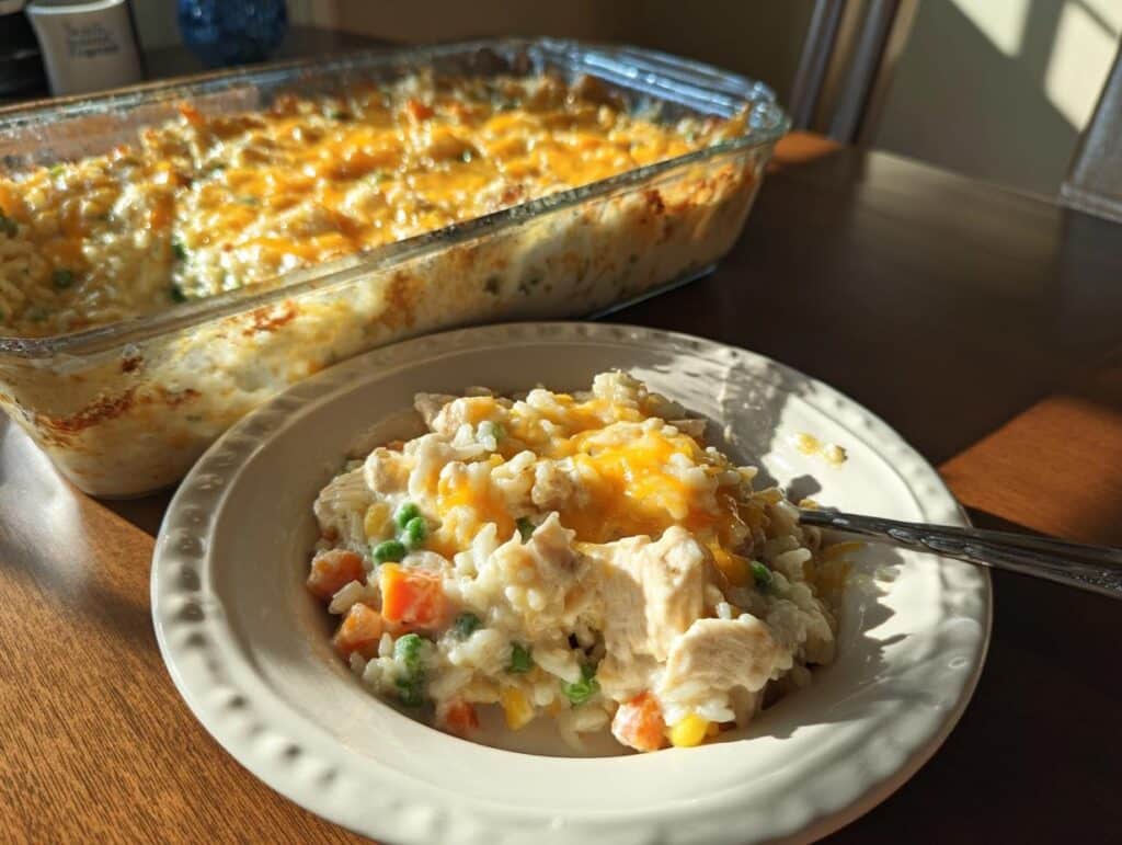 A serving of Pioneer Woman Chicken Rice Casserole on a plate, next to the casserole dish. Cheesy and delicious!