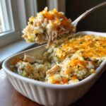 Spoonful of Pioneer Woman Chicken Rice Casserole being lifted from a baking dish, showing chicken, rice, and cheese.