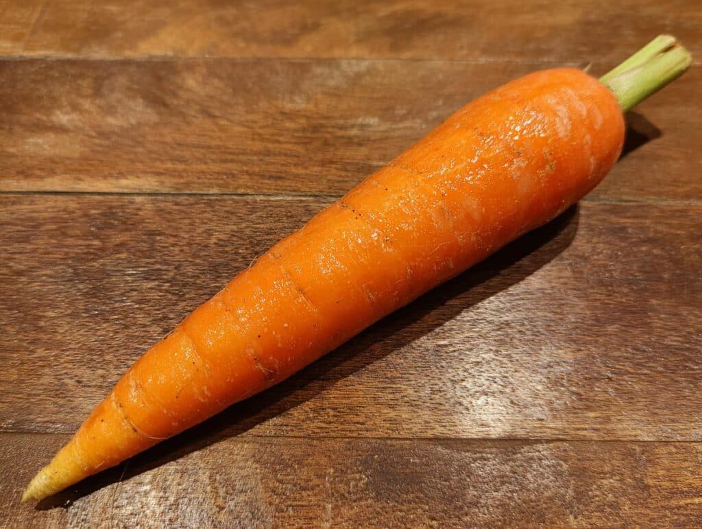 A single, vibrant orange carrot on a wooden surface, ready for a Raw Carrot Salad recipe.