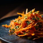 Close-up of vibrant Raw Carrot Salad with shredded carrots and fresh parsley on a dark plate.