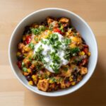 Overhead view of Santa Fe Chicken in a bowl, topped with sour cream and cilantro. Includes chicken, corn, beans, and peppers.