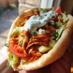 Close-up of a Slow Cooker Chicken Shawarma wrap with chicken, lettuce, tomato, cucumber, and tzatziki sauce.