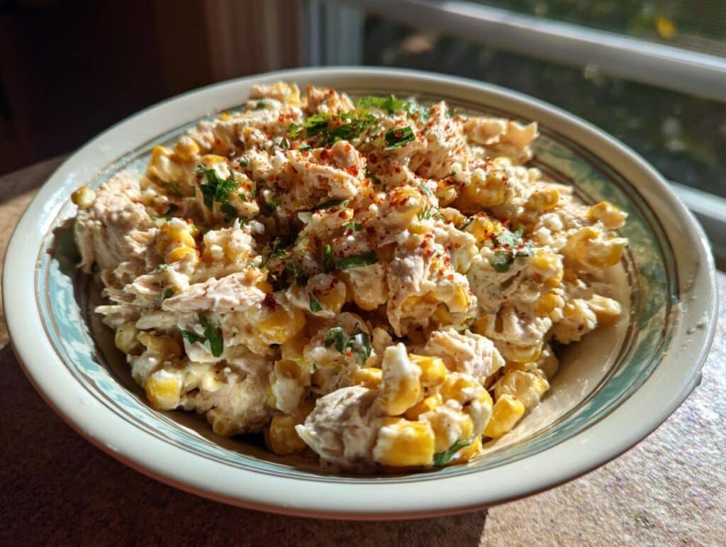 A bowl of creamy Slow Cooker Street Corn Chicken, garnished with herbs and chili powder.