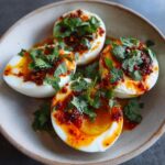 Halved spicy harissa eggs with creamy whipped goat cheese, garnished with fresh cilantro.