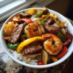A bowl of Steak and Shrimp Stir Fry with colorful bell peppers and onions served over white rice.