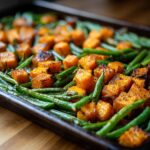 A close-up of a Sweet Potato Green Bean Tray Bake, showcasing roasted sweet potato cubes and green beans on a baking sheet.