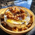 Delicious baked brie cheese topped with honey and walnuts in a ceramic dish.
