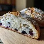A slice of Blueberry Lemon Sourdough Bread on a wooden board, showing blueberries and lemon zest.
