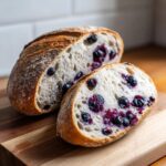 A sliced loaf of blueberry sourdough bread on a wooden board, showing the blueberries inside the bread.