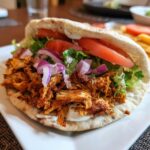 Close-up of Chicken Shawarma in pita bread with tomatoes, lettuce, red onions, and sauce.