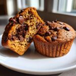 Two chocolate chip muffins on a plate, one cut in half to show the chocolate center.