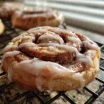 Close-up of a glazed Cinnamon Roll Sugar Cookie on a cooling rack, with more cookies blurred in the background.