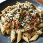 Close-up of creamy chicken pasta with penne, shredded chicken, parmesan, and parsley.