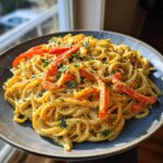 A plate of Creamy Vegan Cajun Pasta, garnished with red bell peppers and fresh herbs.
