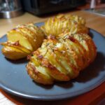 Three crispy potatoes, sliced and baked with herbs, are arranged on a dark plate.