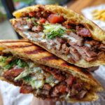Close-up of a Doner Kebab sandwich cut in half, showing layers of meat, lettuce, tomato, and sauce on grilled bread.