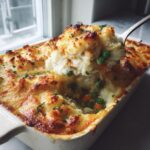 Spoon lifting a portion of easy chicken shepherds pie recipe from a baking dish, showing chicken, peas, and mashed potato topping.