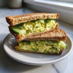 Two halves of an Easy Cucumber Salad Sandwich stacked on a plate, showing the cucumber salad filling and dill.