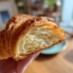 Close-up of a croissant recipes showing flaky layers inside, golden brown crust.