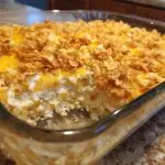 Close-up of funeral potatoes with hashbrowns in a glass baking dish, topped with cornflakes and cheese.