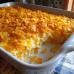 Close-up of funeral potatoes with hashbrowns in a white casserole dish, topped with cornflakes.
