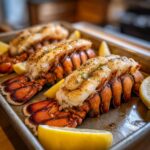 Three Garlic Butter Lobster Tails on a baking sheet, garnished with lemon wedges.