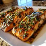 Three fillets of Garlic Butter Salmon on a white plate, glistening with sauce and herbs.