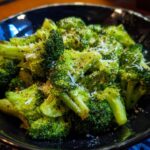 Close-up of Garlic Parmesan Broccoli in a black bowl, sprinkled with parmesan and pepper.