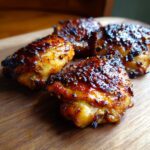 Four glazed chicken thigh recipes on a wooden board, showing crispy skin and a savory glaze.