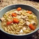 A comforting bowl of Grandma's chicken noodle soup with chicken, noodles, carrots, and celery.