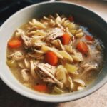 A comforting bowl of Grandma's chicken noodle soup with chicken, noodles, carrots, and celery.