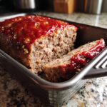 Freshly baked meatloaf with a rich glaze, sliced and ready to serve in a baking pan. Delicious meatloaf recipe.