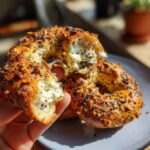 A hand holds a halved high protein bagel with cottage cheese and almond flour, showcasing its texture and filling.