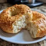 Two homemade protein bagels on a white plate, one bagel torn in half to show the inside texture.