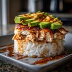 A delicious Honey Lime Chicken and Avocado Rice Stack on a square plate, drizzled with sauce.