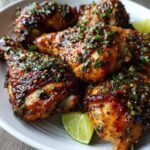 Close-up of Honey Lime Chicken drumsticks on a white plate, garnished with lime wedges and fresh herbs.