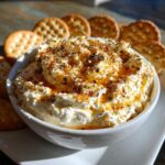 A bowl of creamy Hot Honey Ricotta Dip, drizzled with honey and spices, surrounded by crackers.