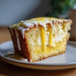 A slice of Lemon Cream Cheese Dump Cake with lemon glaze dripping down the sides on a plate.